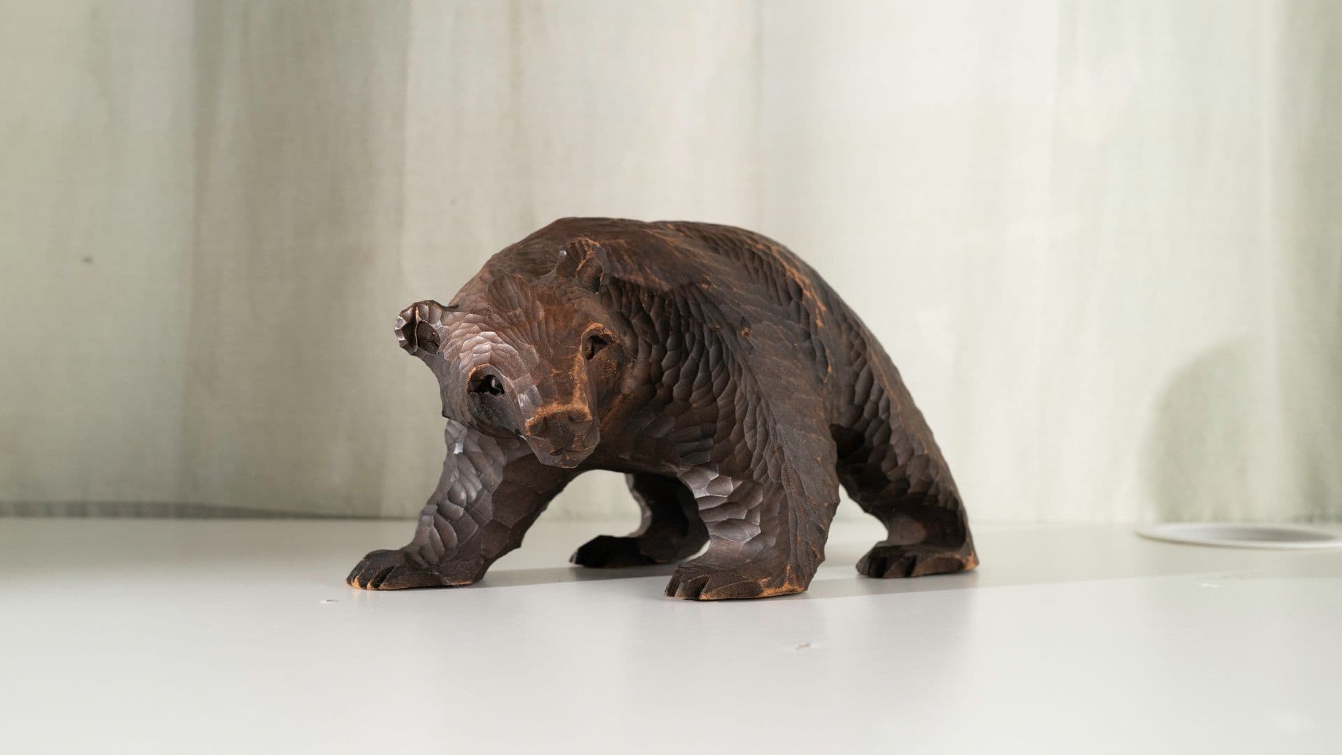 Wooden bear sculpture on white surface with light-colored background