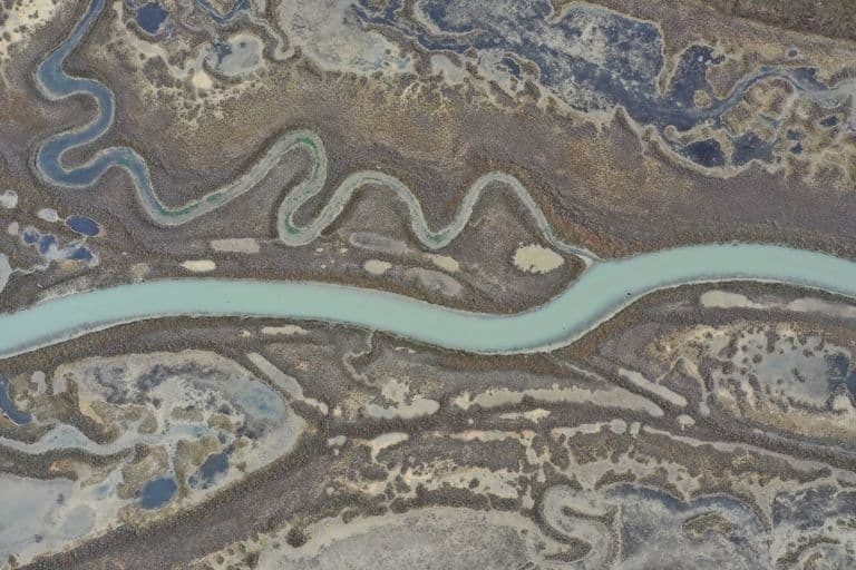 An aerial view of a winding river flowing through a dry, rocky landscape with smaller ponds and tributaries branching off.