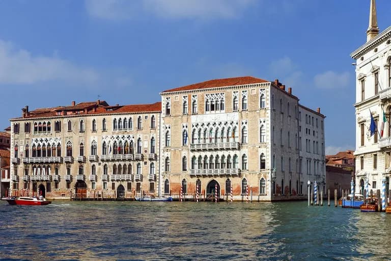 Historic Venetian buildings along a canal with boats, blue sky, and water in Venice, Italy.