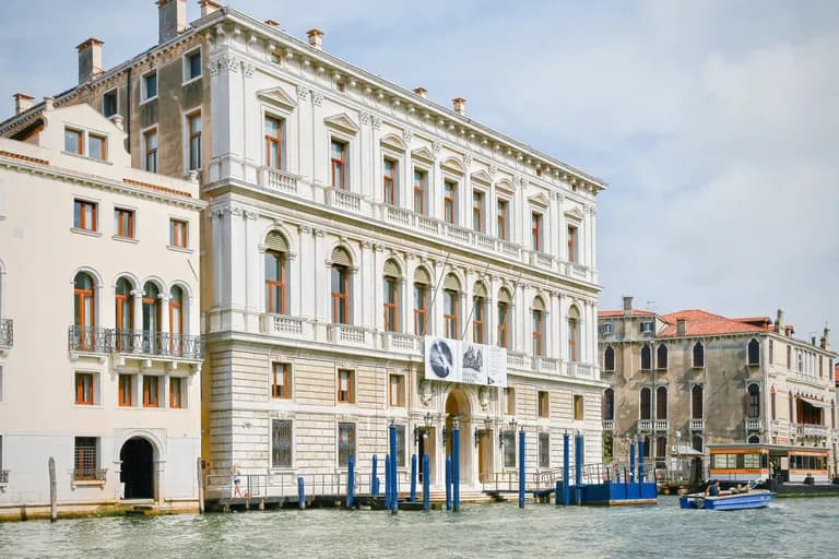 Venetian buildings along a canal with boats, featuring classical architecture and large windows.