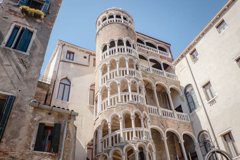 View of the Leaning Tower of Pisa with surrounding historic buildings and clear blue sky.