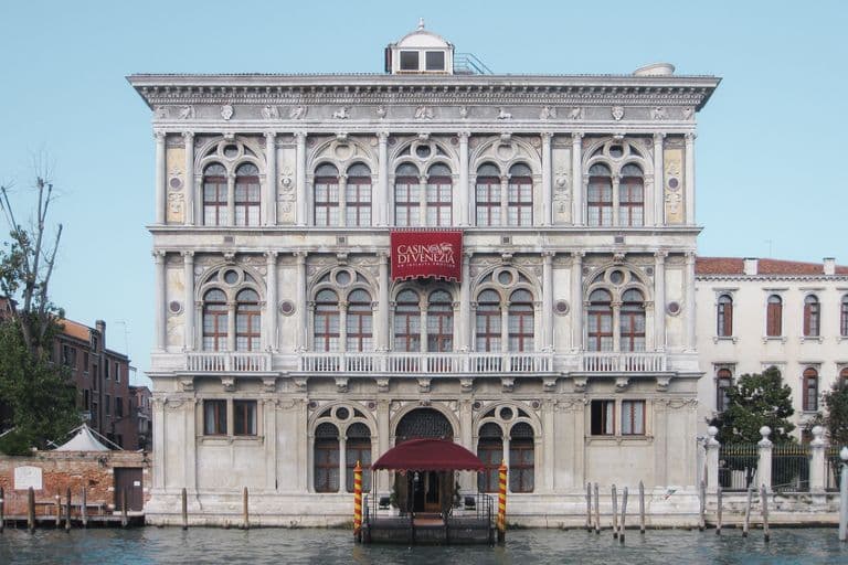 Historic white marble building with arched windows on the Grand Canal in Venice, Italy, with a sign for Casino di Venezia at the front