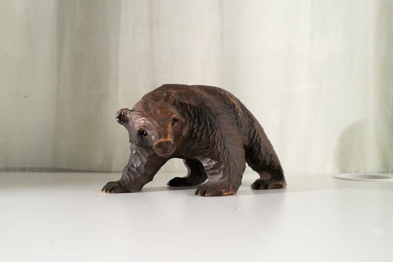 Wooden bear sculpture on white surface with light-colored fabric background.