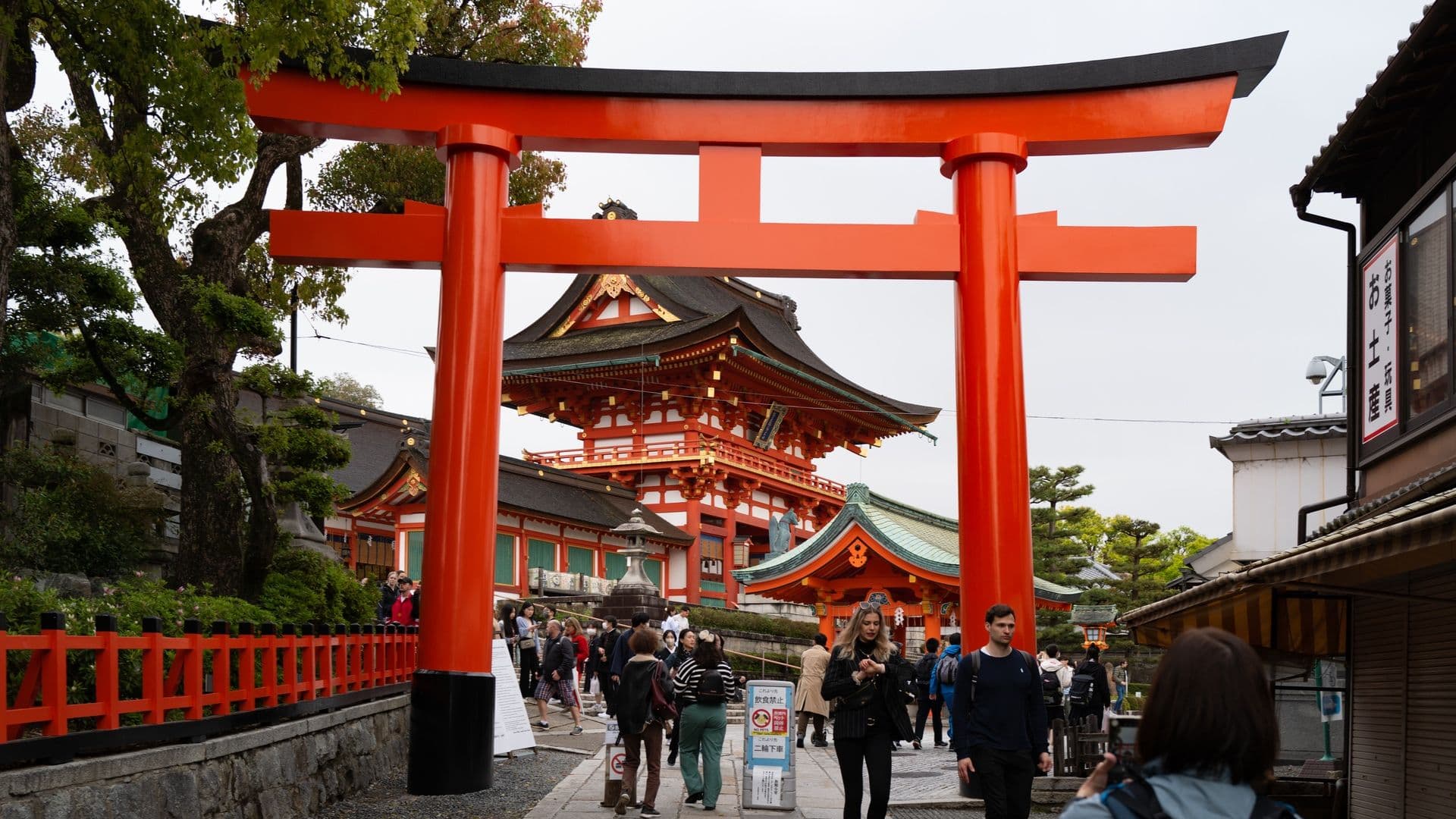 Fushimi Inari Shrine entrance with large red torii gate and tourists walking underneath in Kyoto, Japan.