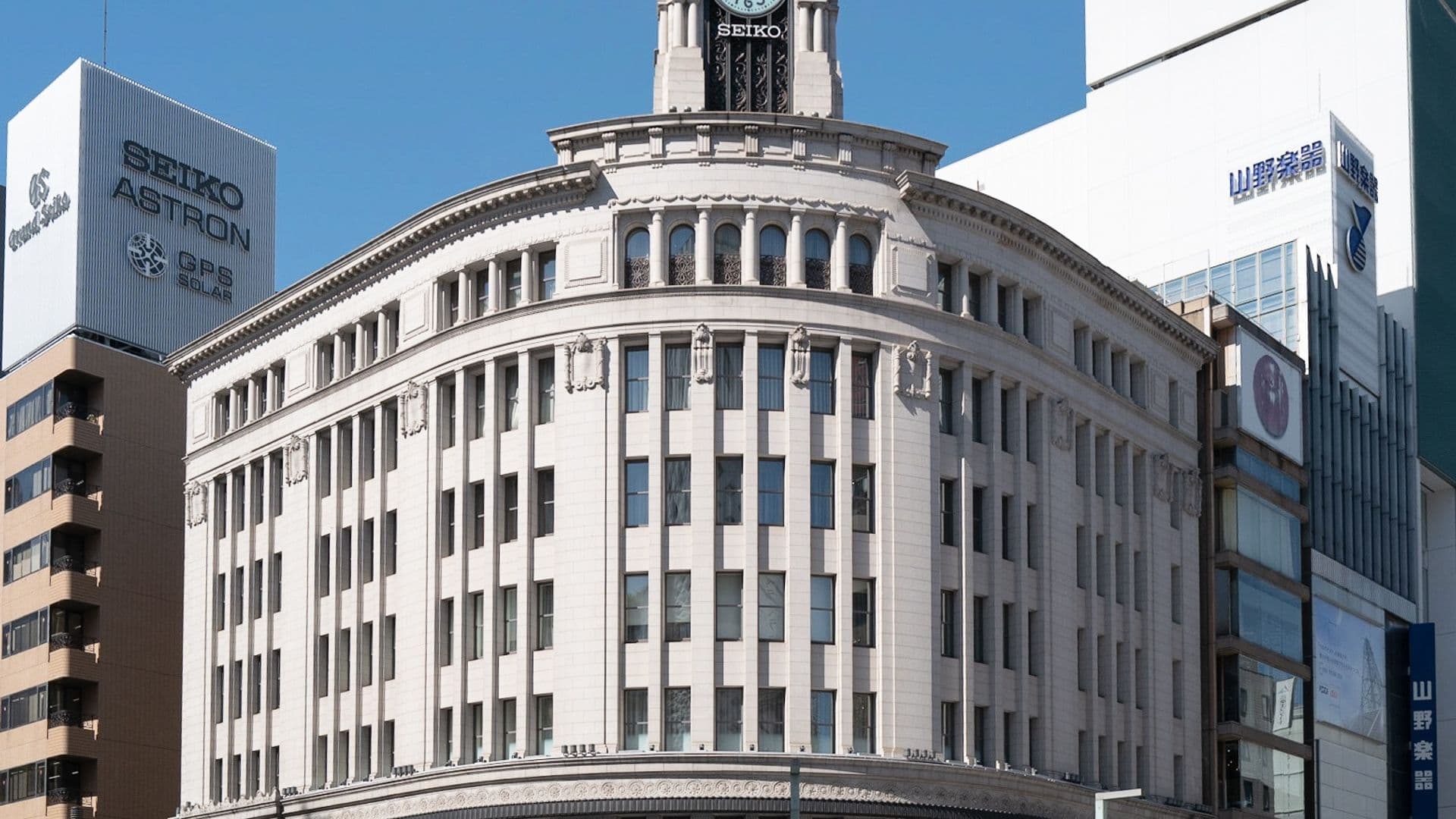 A large historic building with a clock tower on a city street, surrounded by modern buildings and street traffic.